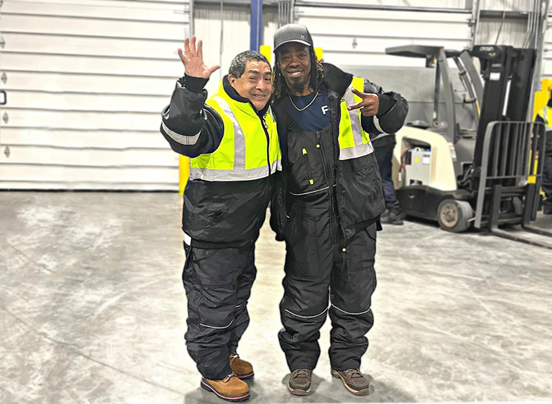 Two FlexCold workers, dressed for the cold and with their arms around each other, smile at the camera